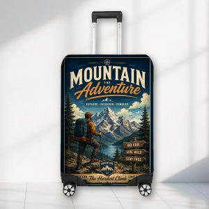 May include: A black rolling suitcase featuring a graphic print of a hiker standing before a mountain range. The text reads MOUNTAIN THE ADVENTURE, EXPLORE DISCOVER CONQUER, GO FAR LIVE WILD STAY FREE, and The Hardest Climb Comes The Best View.