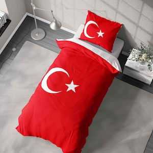 May include: Red bedding set with the Turkish flag design, featuring a white crescent moon and star. The set includes a duvet cover and a pillowcase, both in red. The bedding is on a bed with a white sheet. The room has a grey carpet.