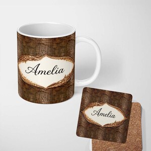 May include: A white ceramic mug and a square coaster featuring a brown textured pattern resembling reptile skin. Both items display a central cream-coloured scalloped label with the name Amelia printed in a black cursive script font.