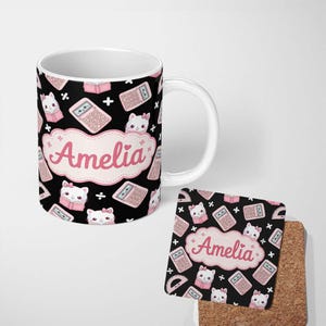 May include: A white ceramic mug and a square cork-backed coaster featuring a black background with a repeating pattern of pink calculators, books, and white cats with pink bows. A central pink scalloped label displays the name Amelia in pink.