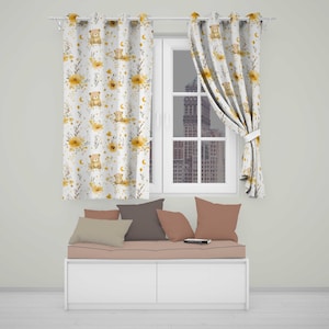 May include: Two white curtains featuring a repeating pattern of light brown teddy bears, yellow flowers, green foliage, and small yellow crescent moons. The curtains are hung on a silver rod with metal grommets, framing a window with a city view.