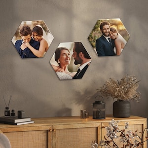 May include: Three hexagonal wall art pieces showing wedding photographs. The images depict couples in formal attire, embracing each other. The art is mounted on a neutral wall, with a wooden cabinet and decorative items in the foreground.