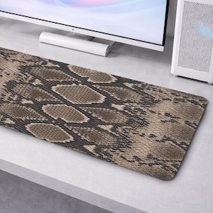 May include: A rectangular desk mat featuring a detailed, repeating snakeskin pattern in shades of brown, tan, and black. The surface displays a textured, scaled appearance that mimics the natural skin of a snake across the entire mat.