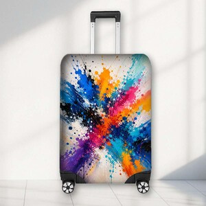 May include: A rolling suitcase featuring a vibrant, multi-coloured paint splatter design on its front panel. The pattern includes splashes of orange, blue, pink, purple, and black against a white background. It has a retractable handle and wheels.