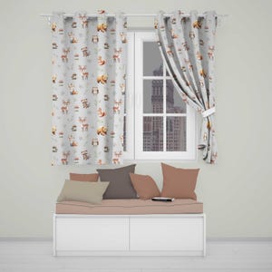 May include: Light grey curtains featuring a repeating pattern of woodland animals including deer, bears, foxes, raccoons, and owls, paired with a white window frame, a white storage bench, and several solid-coloured throw pillows in shades of tan and brown.