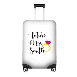 May include: A white suitcase cover featuring the text "future Mrs. Smith" in black script, and a pink diamond ring with a yellow band. The suitcase has a retractable handle and black wheels.