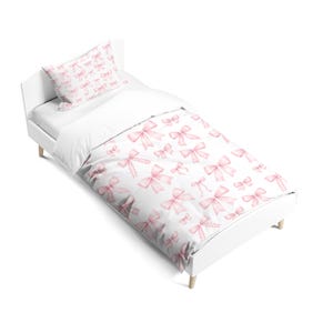 May include: A single bed frame featuring a white mattress and bedding set. The duvet cover and matching pillowcase are decorated with a repeating pattern of light pink watercolour-style bows scattered across a clean white background.