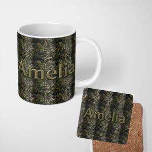 May include: A white ceramic mug and a square cork-backed coaster, both featuring a dark green and black reptilian scale pattern. The name Amelia is printed in a metallic gold, embossed-style font on the centre of both the mug and the coaster.