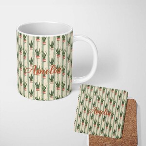 May include: A white ceramic mug and a square cork coaster featuring a repeating pattern of green potted plants on vertical light green stripes. The name Amelia is printed in a cursive orange font on the centre of both the mug and the coaster.