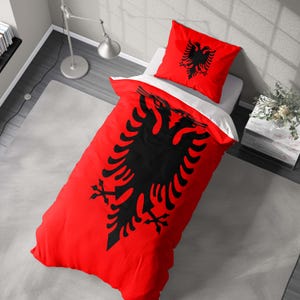 May include: A red and black bedding set with a large black eagle design. The set includes a duvet cover and a pillowcase. The bedding is on a white bed. The duvet cover and pillowcase feature the same design. The background includes a gray rug and a lamp.