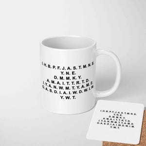 May include: A white ceramic mug with a curved handle and a matching coaster. Both items feature black text arranged in a circular pattern. The text includes a series of letters and abbreviations. The mug and coaster are on a white surface.