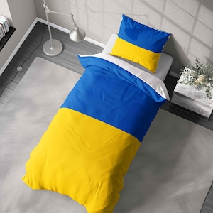 May include: A blue and yellow duvet cover and pillow set. The bedding features a design with a blue top half and a yellow bottom half. The pillow has a similar design. The bedding is on a white bed.