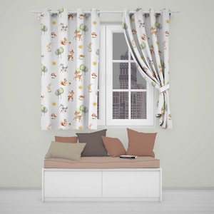 May include: White curtains featuring a repeating watercolour pattern of brown deer, grey wolves, squirrels, rabbits, green trees, and yellow suns. The curtains hang on a rod above a white storage bench with a light pink cushion and four throw pillows.