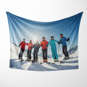 May include: A group of five people wearing winter sports clothing and ski gear are standing on a snowy mountain slope. They are holding skis and ski poles. The sky is blue and there is a bright sun shining in the background.