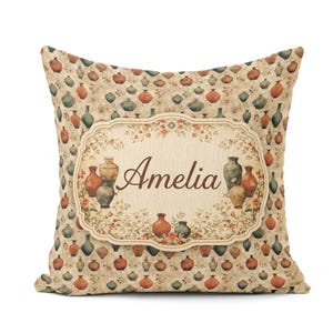 May include: A square throw pillow featuring a repeating pattern of small, colourful vases on a beige background. In the centre, a decorative scalloped label displays the name Amelia in brown script, surrounded by floral vines and vase illustrations.