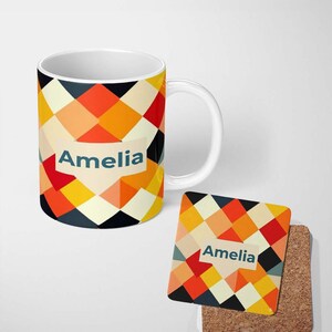 May include: A white ceramic mug and a square cork-backed coaster featuring a geometric pattern of red, orange, yellow, and black diamonds. Both items display a cream-coloured label with the name Amelia printed in dark blue sans-serif text.
