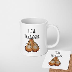 May include: White ceramic mug with the text "I LOVE TEA BAGGING" and a cartoon illustration of testicles. A matching coaster with the same design is also present.