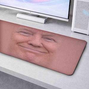 May include: A rectangular mouse mat with a close-up of a smiling face. The mat has a black border and a light skin-toned background. The image is of a person with a slight smile.