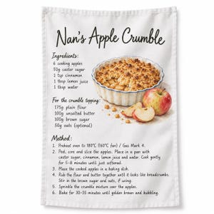 May include: A white tea towel featuring the text Nan's Apple Crumble, a list of ingredients, and a recipe method. The design includes a watercolour illustration of a baked apple crumble in a fluted dish, alongside a whole red apple and two slices.