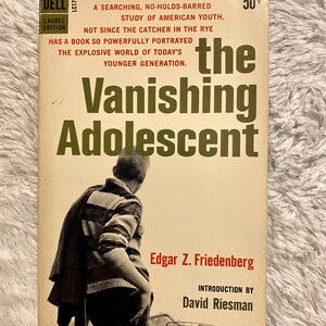 May include: A vintage paperback book cover with a black and white photo of a young man wearing a striped sweater. The title is "The Vanishing Adolescent" by Edgar Z. Friedenberg with an introduction by David Riesman.