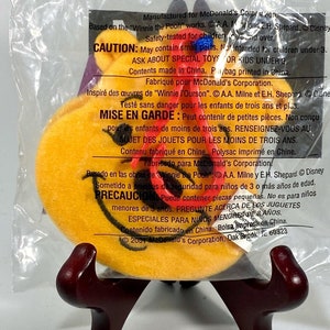 May include: A yellow plush Winnie the Pooh character with a red nose and a smile. The character is packaged in a clear plastic bag with a red and white warning label. The label includes the text "Caution: May contain small parts. Not intended for children under 3. Ask about special toys for kids under 3." The label also includes the text "Contents made in China. P/bag printed in China."