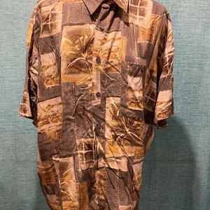 Puede incluir: Una camisa de manga corta con botones y un estampado abstracto marrón y beige. La camisa tiene cuello y un solo bolsillo en el pecho.