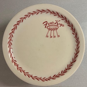 May include: White ceramic plate with a red border of stylized leaves. The center of the plate has the words "Four Keys Restaurant" in red lettering.