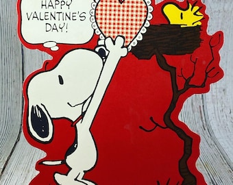 May include: A red Valentine's Day card featuring Snoopy holding a red and white gingham heart. The card has the text "Happy Valentine's Day!" and is signed "Schulz".
