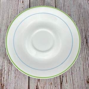 Puede incluir: Un platillo blanco con un borde verde y azul. El platillo est&aacute; hecho de cer&aacute;mica y tiene un acabado liso y brillante.