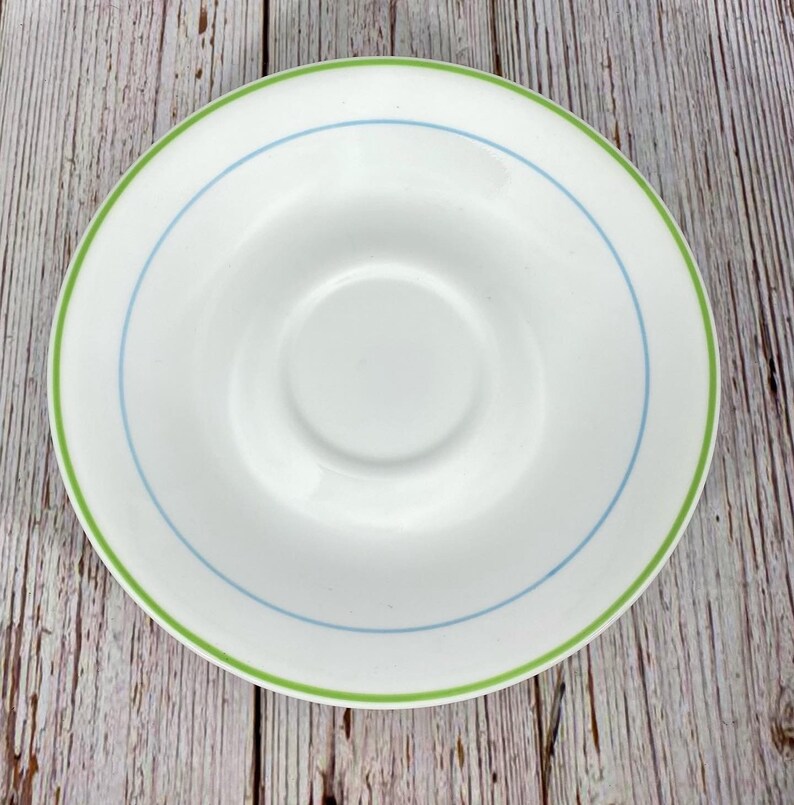 Puede incluir: Un platillo blanco con un borde verde y azul. El platillo est&aacute; hecho de cer&aacute;mica y tiene un acabado liso y brillante.