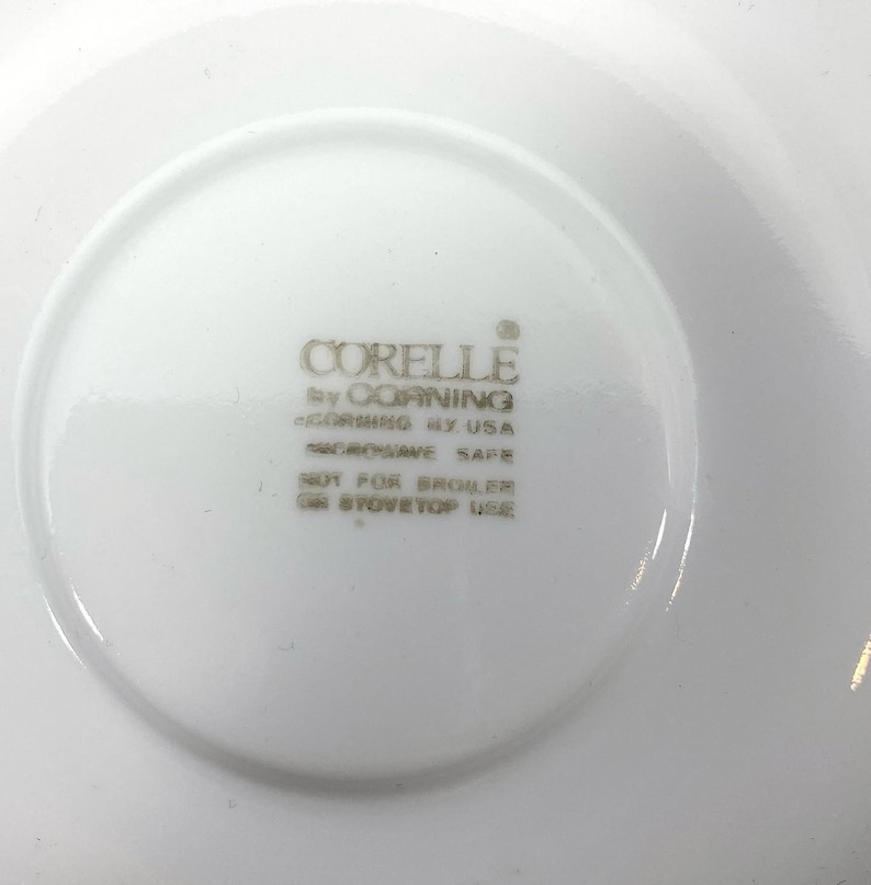 Puede incluir: Plato blanco con el texto "CORELLE by CORNING CORNING BY USA MICROWAVE SAFE NOT FOR BROILER OR STOVETOP USE" impreso en la parte inferior.