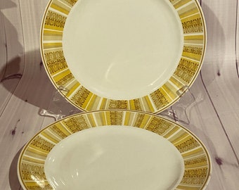 Puede incluir: Dos platos de cena de cerámica blanca con un patrón geométrico amarillo y marrón alrededor del borde.