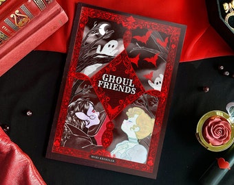 May include: A red and black comic book titled "Ghoul Friends" by Mari Krieller. The cover features two characters, a woman with dark hair and a woman with blonde hair, in a spooky forest setting with bats and ghosts.
