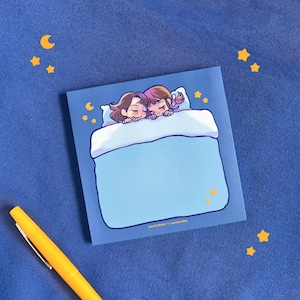 May include: A blue notepad with a cartoon illustration of two people sleeping in a bed with stars and a crescent moon. The text "martwriter x wanderlust" is at the bottom of the notepad.
