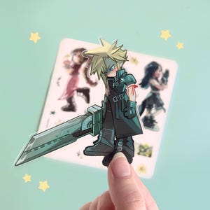 May include: A clear sticker featuring a cartoon illustration of Cloud Strife from Final Fantasy VII, holding a large sword. The sticker has a light blue background with yellow star accents and images of other characters.