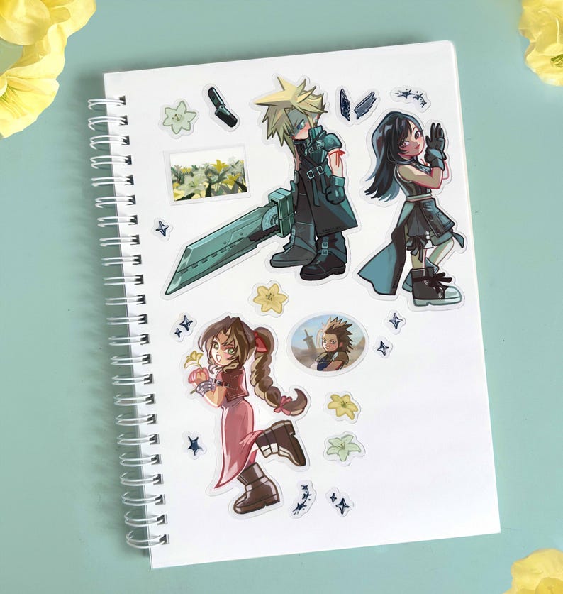 May include: White spiral-bound notebook adorned with colorful stickers featuring anime-style characters. The stickers depict figures with spiky blonde hair, black hair, and various outfits, along with floral and star-shaped accents. The notebook is on a light blue surface.