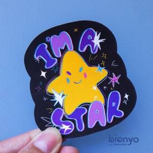May include: A black and purple sticker with a yellow star in the center. The star has a smiling face and is surrounded by white and purple stars. The text "I'm a star" is written in purple and white letters around the star.