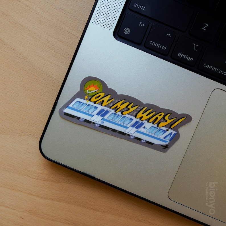 Puede incluir: Una pegatina de tren gris y azul con un sol amarillo y el texto "On My Way!" en un port&aacute;til plateado.