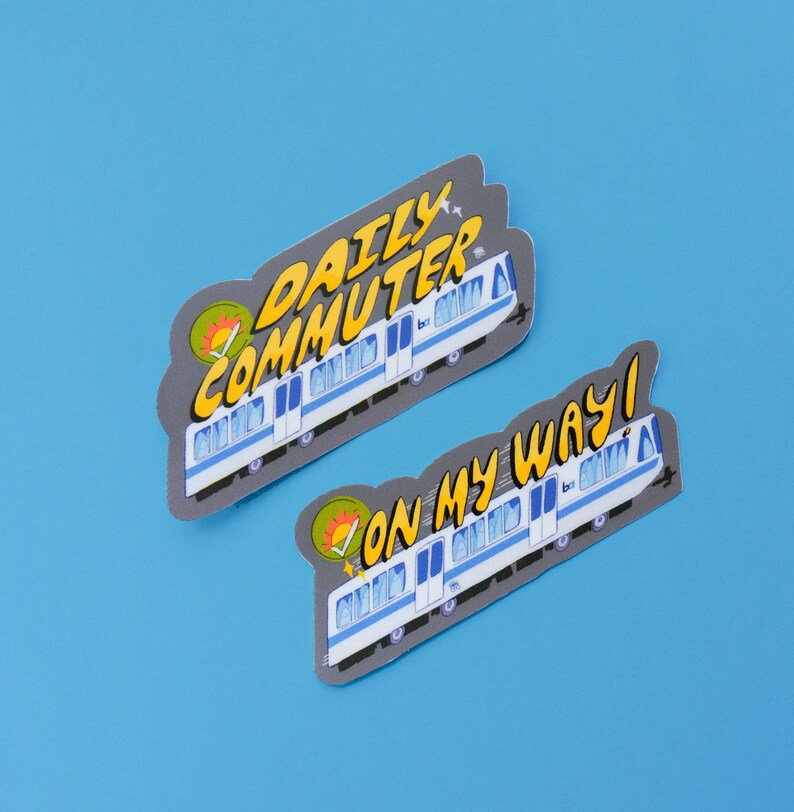 Puede incluir: Dos pegatinas con un tren de dibujos animados con el texto "Daily Commuter" y "On My Way!" en un estilo de c&oacute;mic colorido.