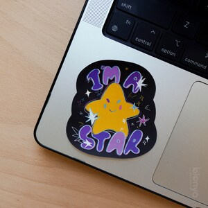 May include: A black and purple sticker with a yellow star and the text "I'm a Star" on a laptop.