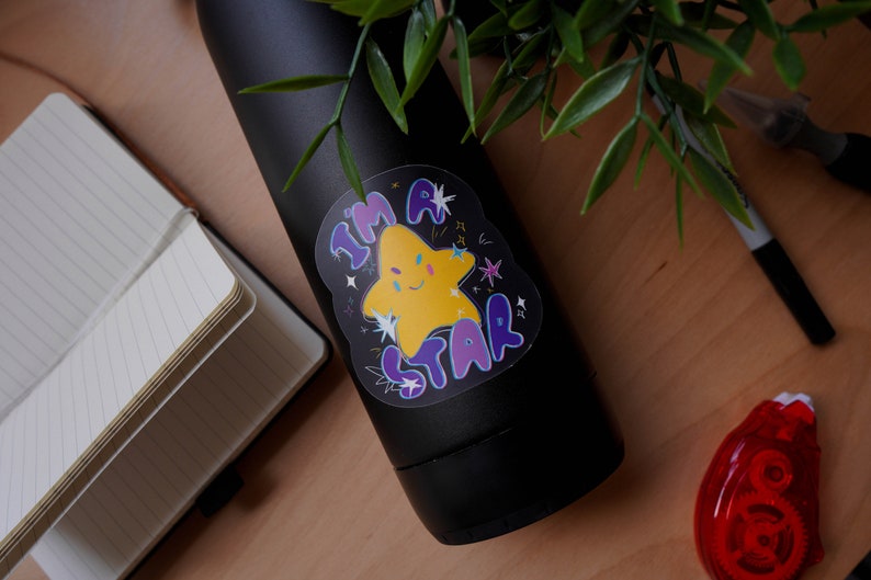 May include: A black water bottle with a sticker that says "I'm a Star" with a yellow star with a face and purple and blue lettering.