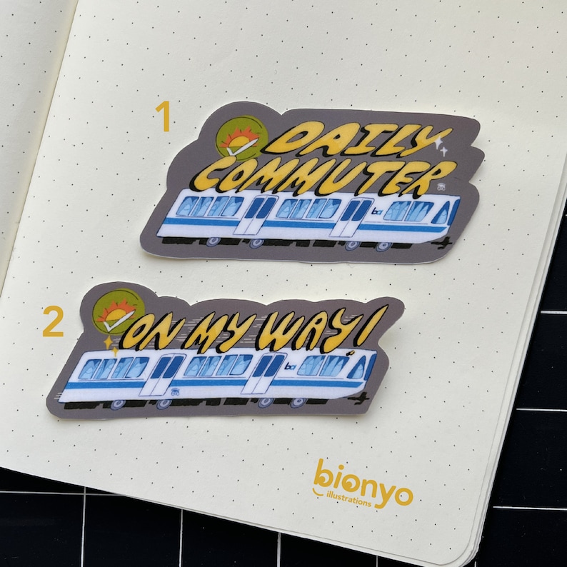 Puede incluir: Dos pegatinas con un tren de dibujos animados con el texto "Daily Commuter" y "On My Way!" Las pegatinas est&aacute;n en una p&aacute;gina de cuaderno blanca con puntos.