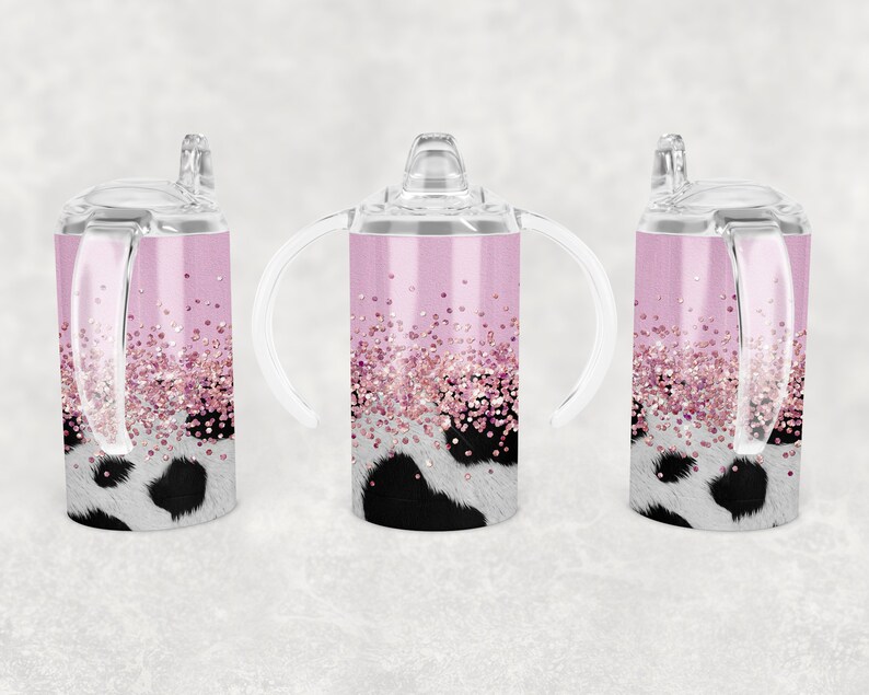 K&ouml;nnte beinhalten: Drei rosa Edelstahl-Trinkbecher mit klaren Deckeln und Griffen. Die Becher haben ein Kuhmuster mit rosa Glitzerakzenten.