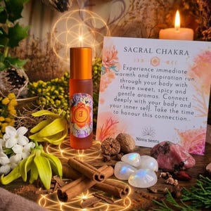 May include: An orange essential oil roller bottle with a label featuring the Sacral Chakra symbol, surrounded by flowers, crystals, and cinnamon sticks. A card reads "SACRAL CHAKRA" and describes the product.