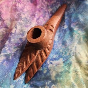 May include: A hand-carved wooden pipe featuring a smooth, tapered stem and a cylindrical bowl. The body of the pipe is decorated with a series of parallel, recessed grooves that resemble leaf veins, showcasing the natural brown wood grain.