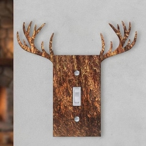 May include: A rectangular light switch cover plate featuring a brown and black marbled texture with two prominent deer antlers extending from the top sides. The plate is secured with two silver screws and contains a single white toggle switch.