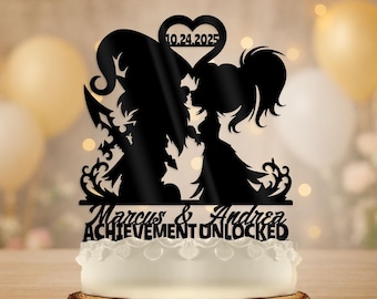 May include: Black silhouette cake topper featuring a couple kissing, with the date 10.24.2025 inside a heart. The names "Marcus & Andrea" and the phrase "ACHIEVEMENT UNLOCKED" are below the figures. The topper is placed on a white cake.