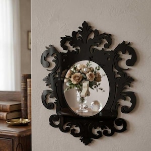 May include: Black decorative light switch cover with an ornate, scrollwork design. The cover surrounds a round mirror with a light switch in the center, labeled "OFF". A vase of flowers is reflected in the mirror.