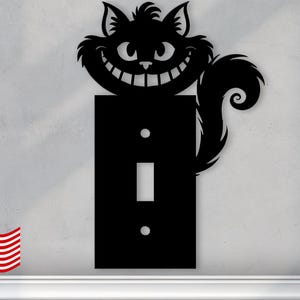 May include: Black light switch cover with a silhouette of a Cheshire Cat from Alice in Wonderland. The cat has a wide grin and a long tail.