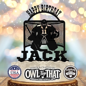Puede incluir: Topper de pastel de acrílico negro con un portero de hockey frente a una red. El topper dice "Feliz cumpleaños Jack" y "Owl Top That".